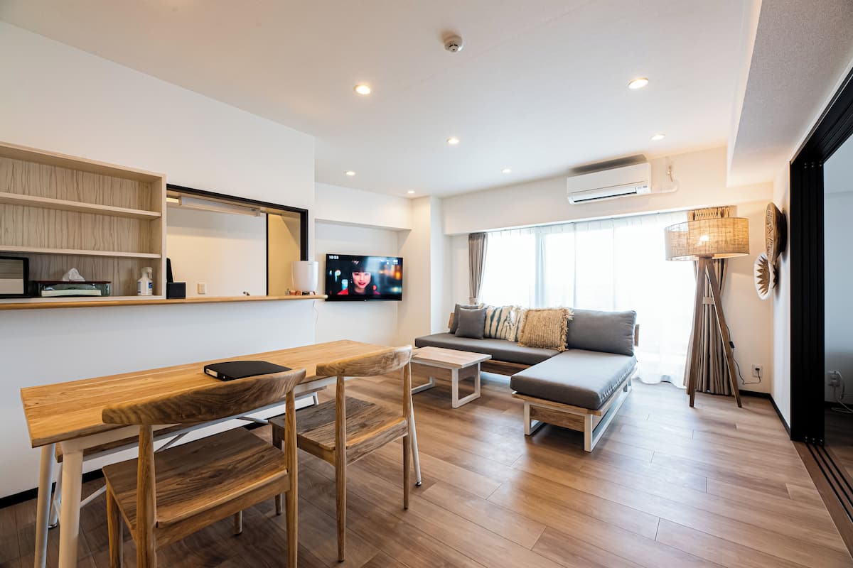 A modern living room with a wooden dining table, a sofa, and a TV mounted on the wall.