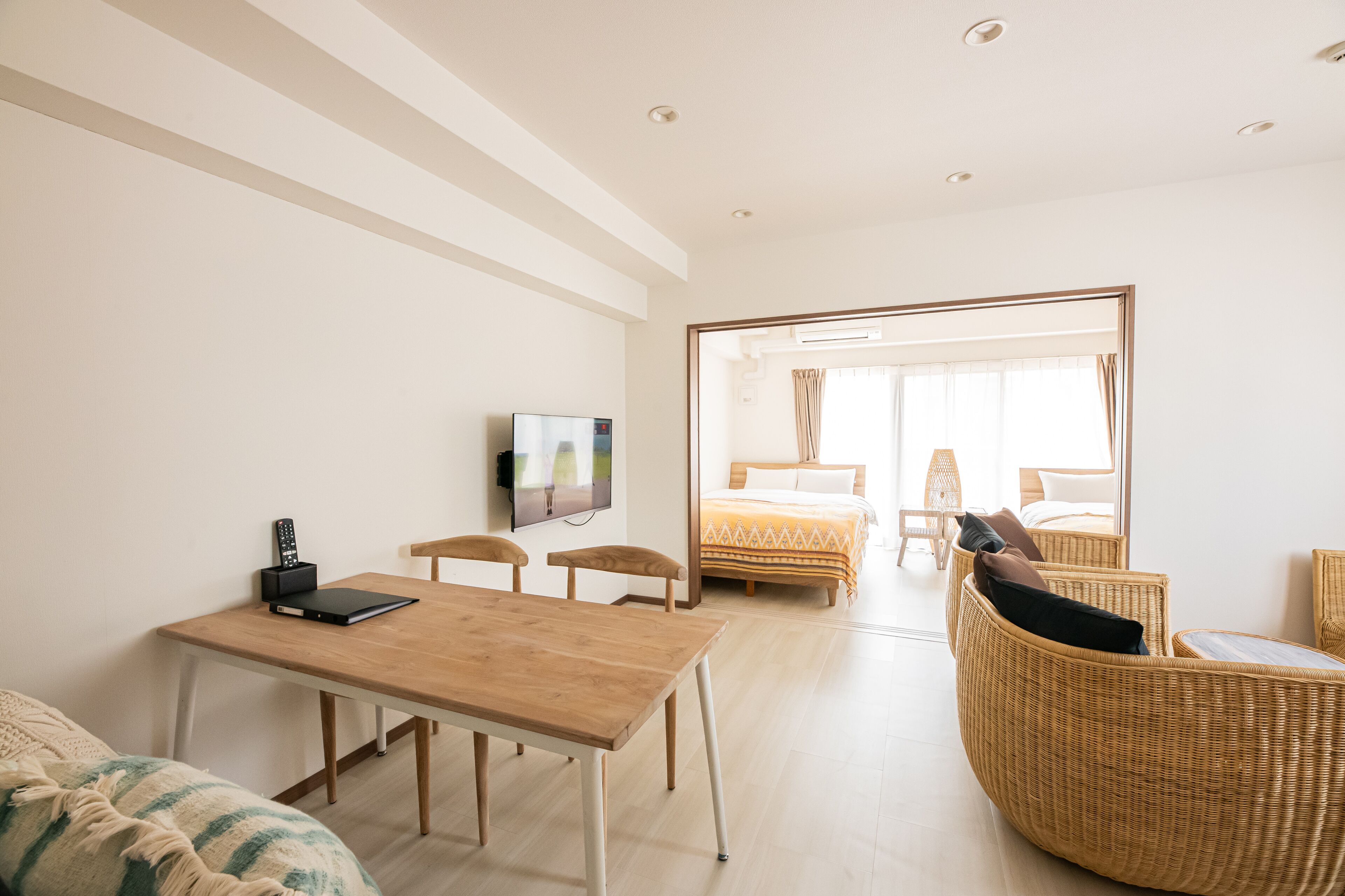 A modern hotel room with a wooden table, a TV, a bed with a view, wicker furniture, and a large mirror.