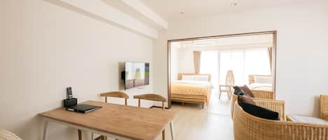 A modern hotel room with a wooden table, a TV, a bed with a view, wicker furniture, and a large mirror.