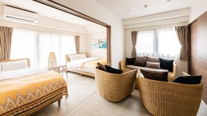 Een hotelkamer met een bed, twee rotan stoelen, een bank en een groot raam.