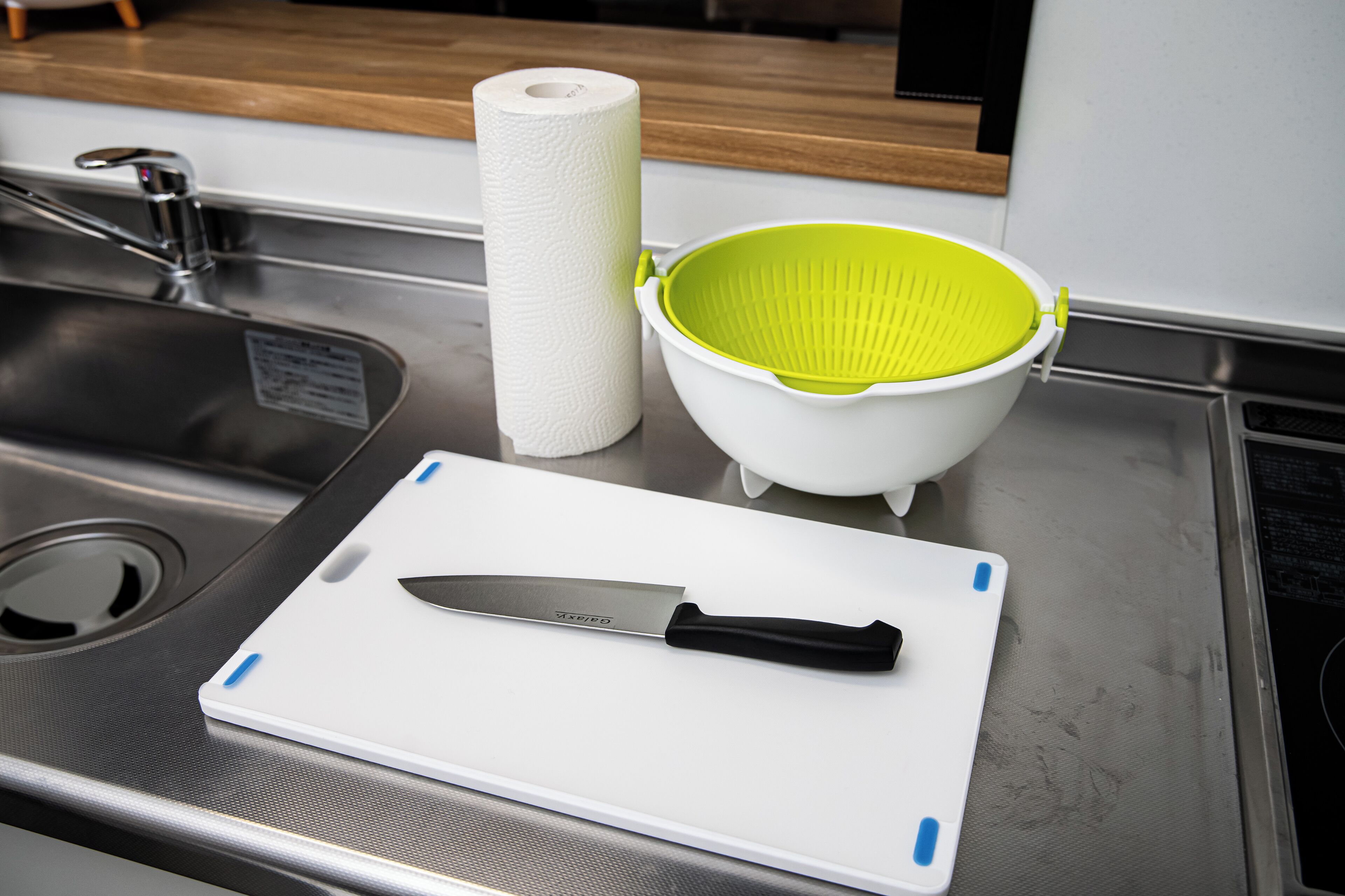 Una encimera de cocina con una tabla de cortar, un cuchillo, un rollo de papel de cocina y un colador.