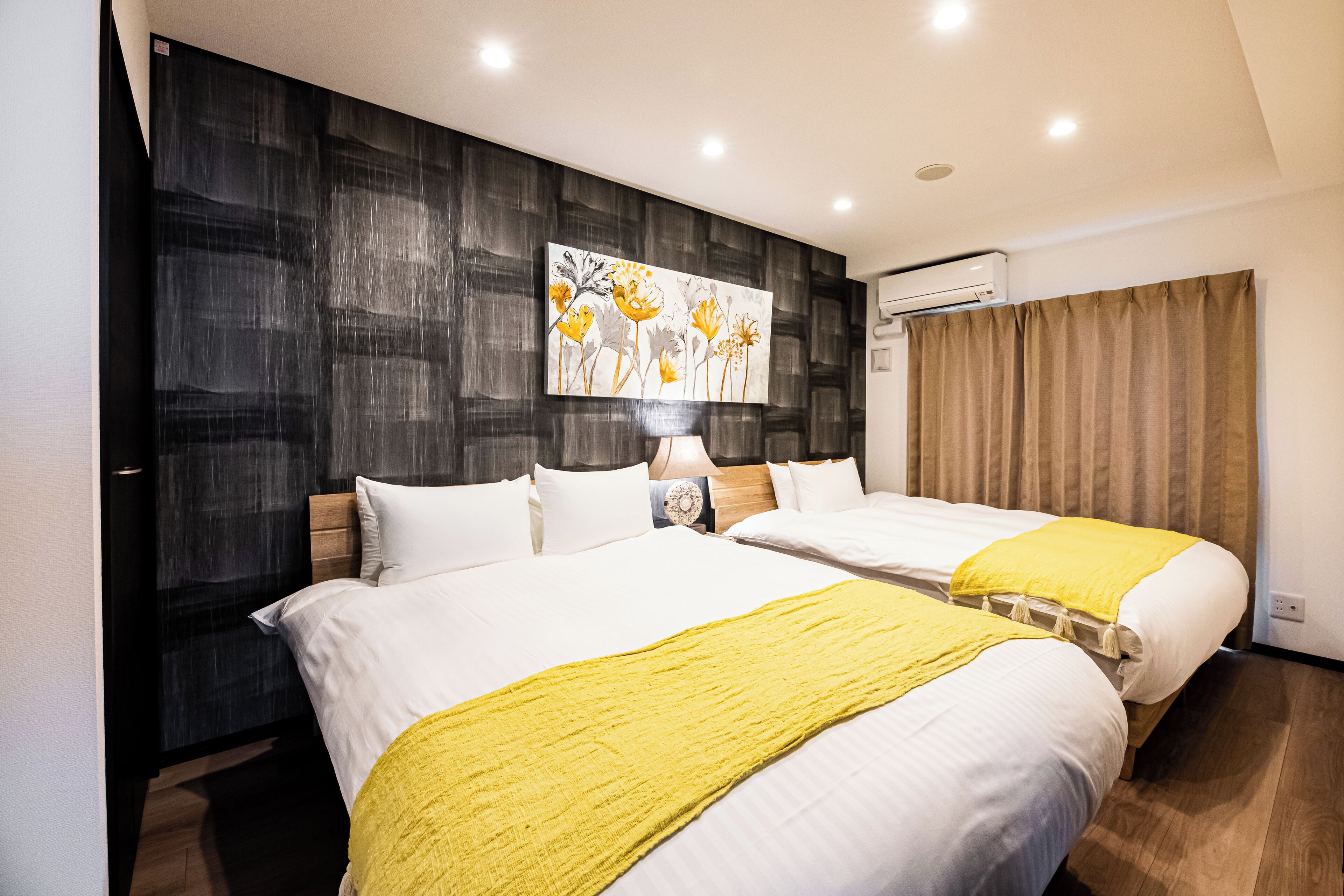 A hotel room with two beds, a large painting on the wall, an air conditioning unit, and a window with curtains.
