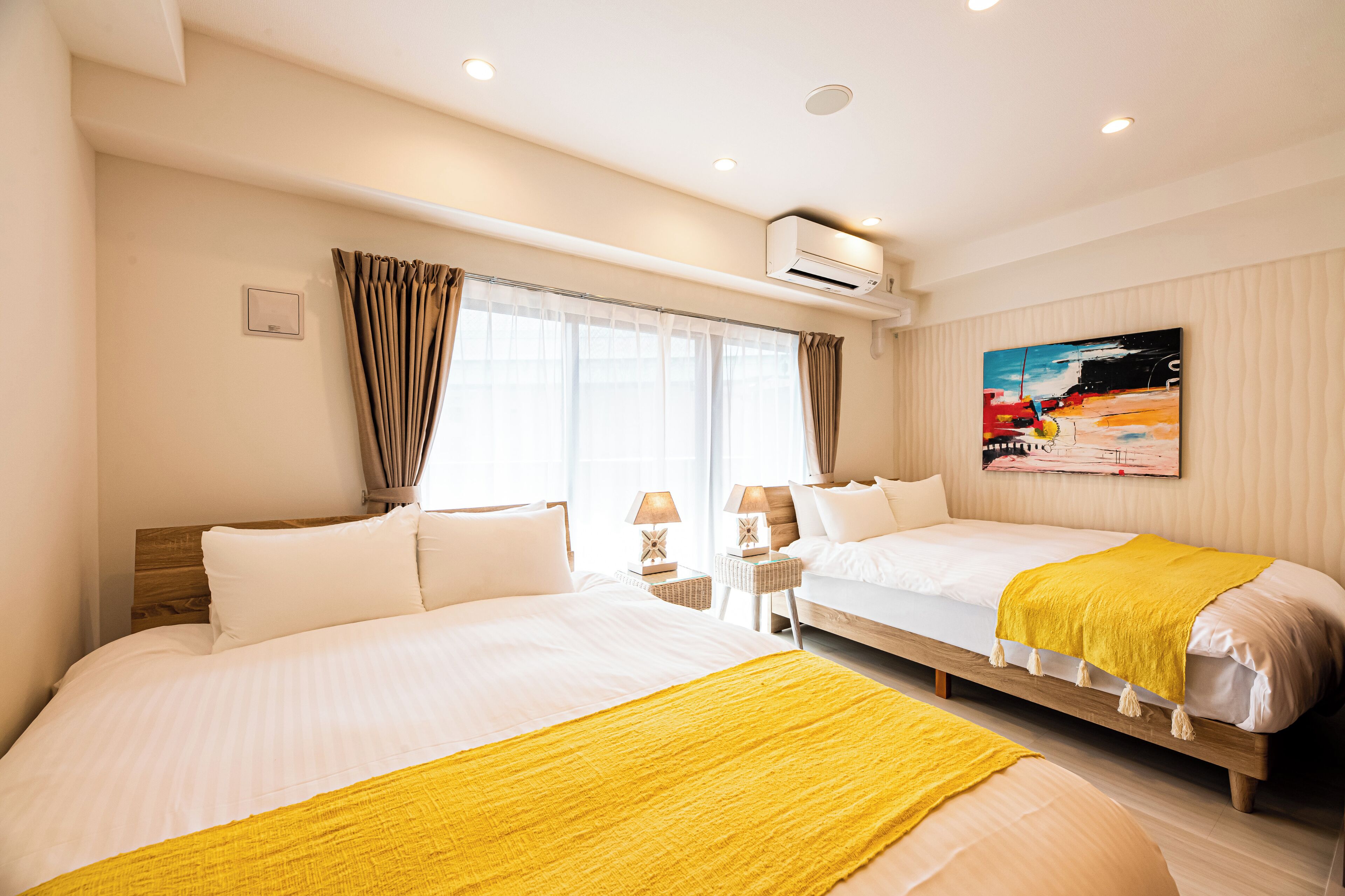A hotel room with two beds, a painting on the wall, and an air conditioning unit.