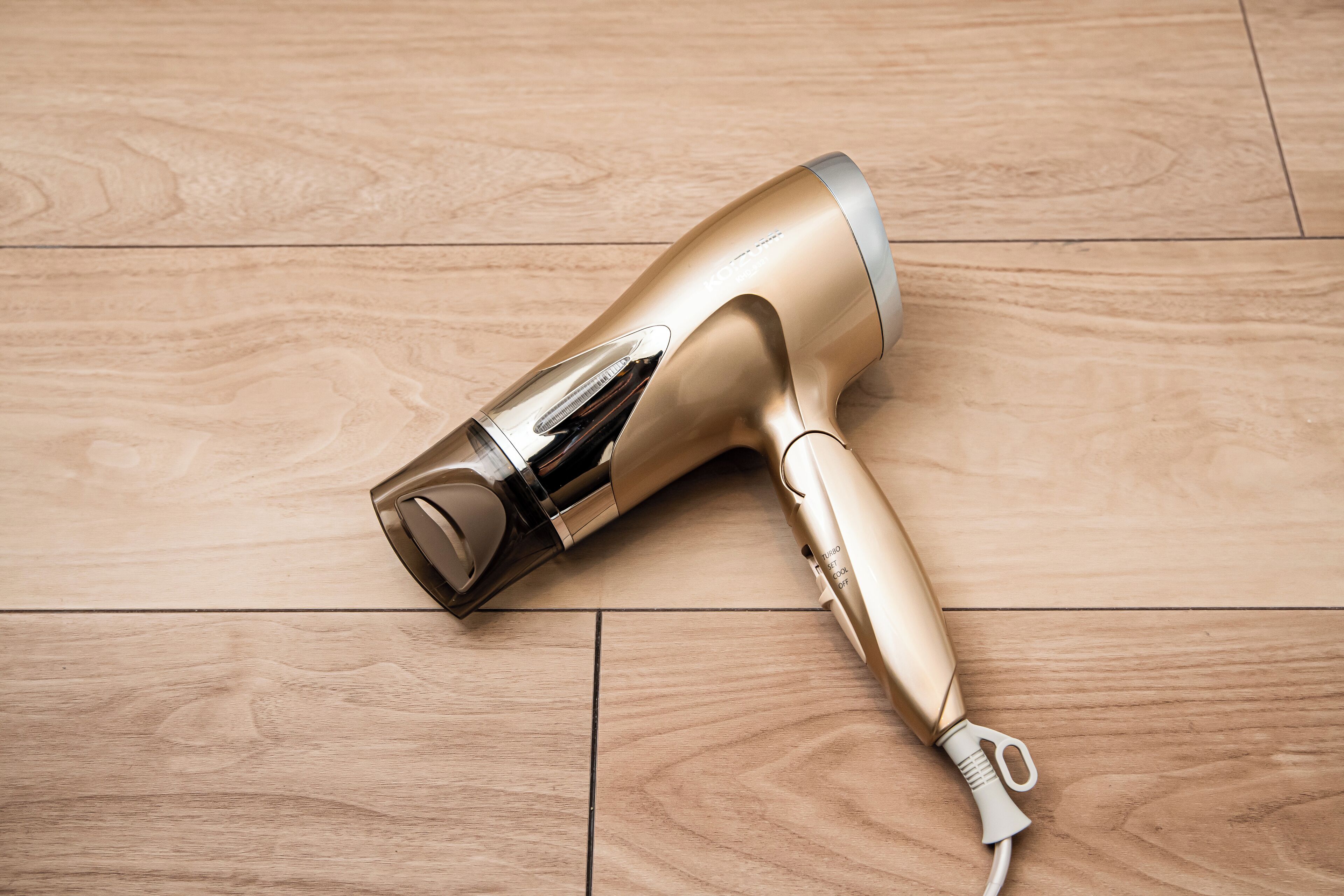 A gold-colored hair dryer on a wooden floor.