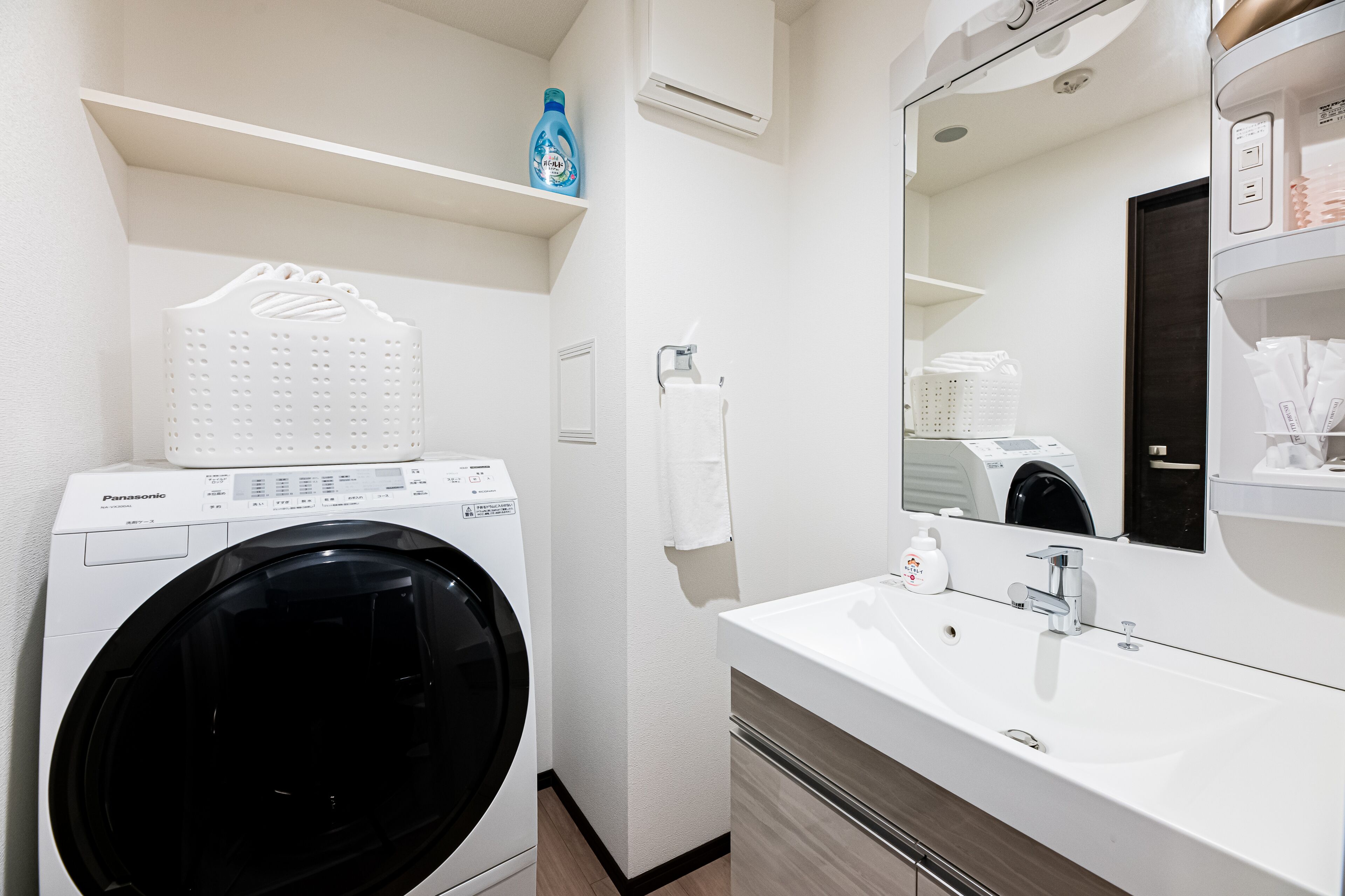 Een moderne badkamer met een wasmachine, een wastafel en een spiegel.