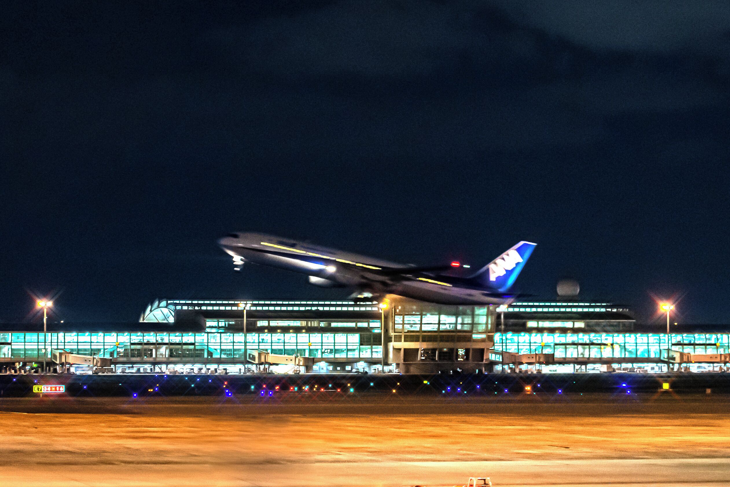 An airplane taking off at night with airport buildings in the background.