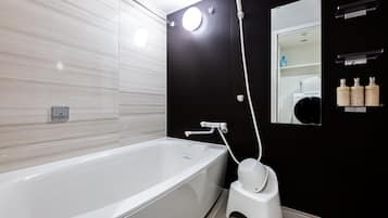 A modern bathroom with a white bathtub, a black wall, a round mirror, and a shelf with toiletries.