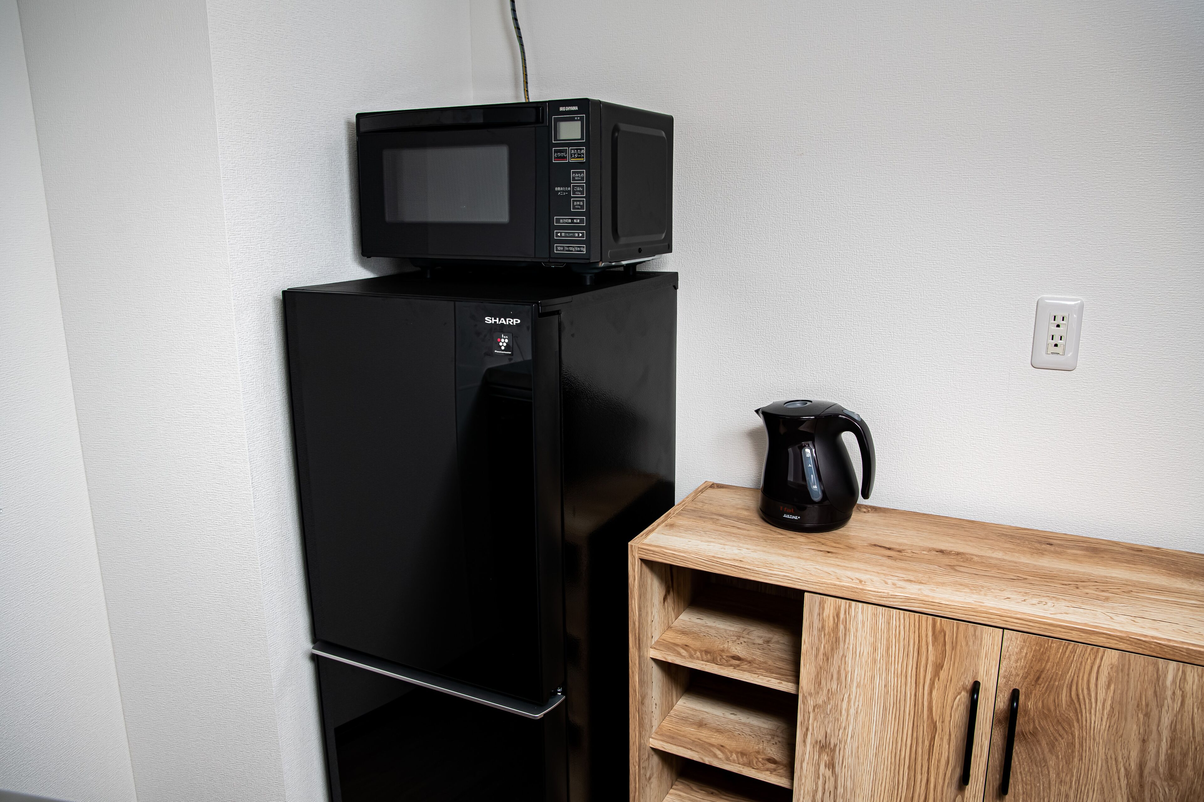 A black refrigerator with a microwave on top, a black coffee maker, and a wooden cabinet with drawers.