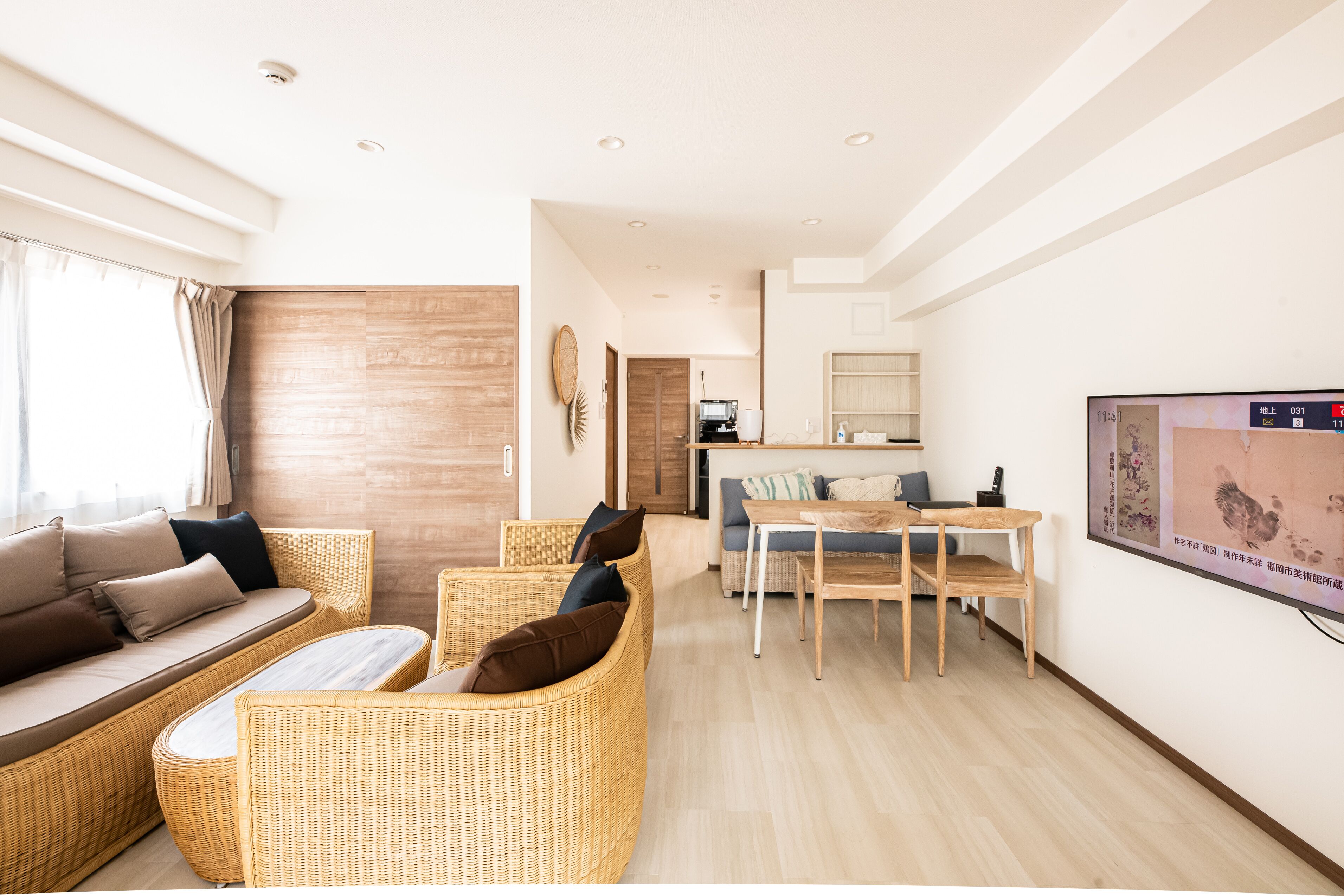 A modern living room with wicker furniture, a dining area, and a kitchen in the background.