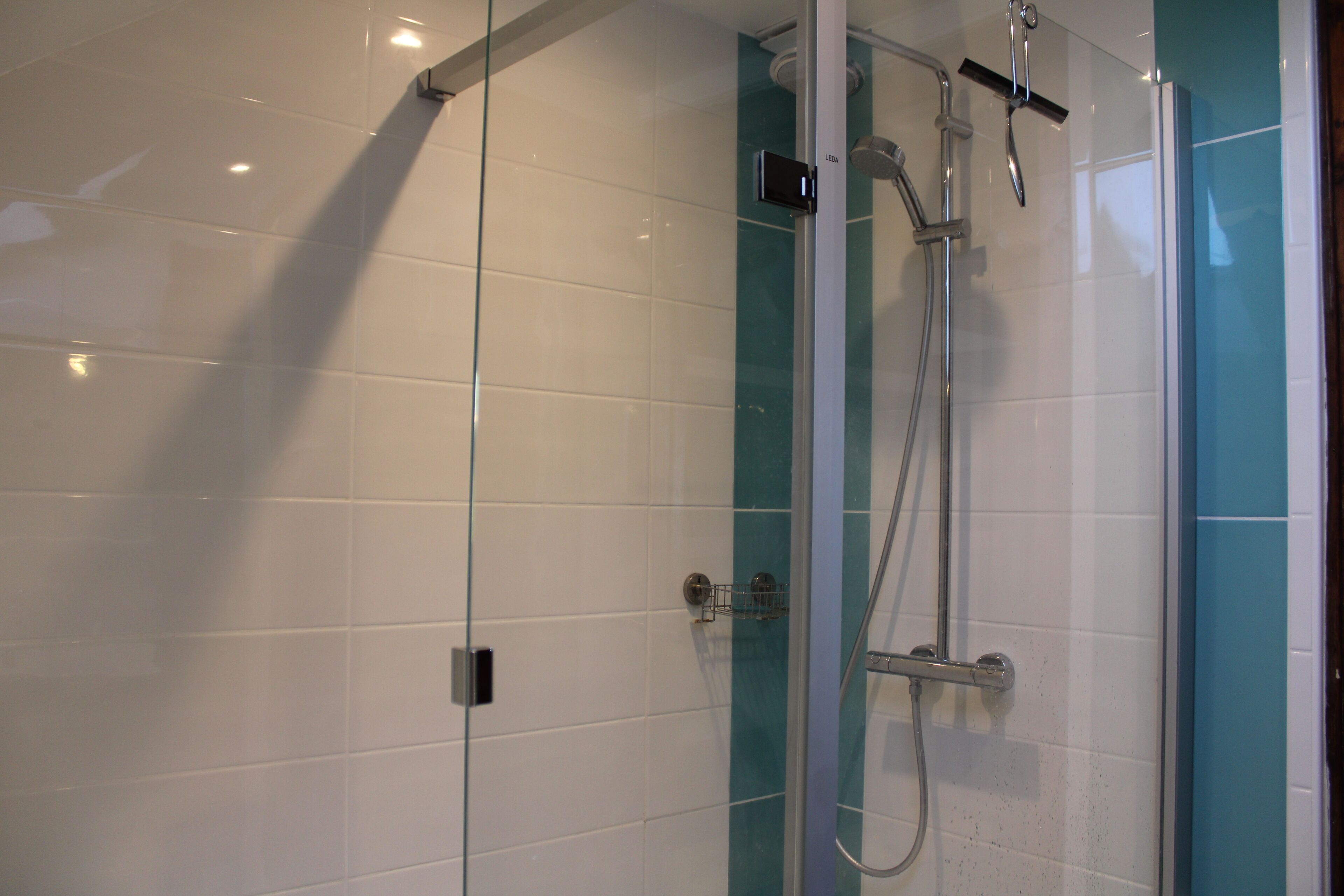 A glass-enclosed shower area with a control panel and a handheld showerhead.