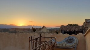 Terraza en la azotea con barandilla metálica, un banco acolchado y vistas a montañas al atardecer.