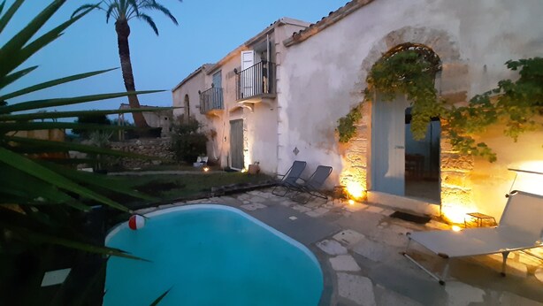 Un patio con piscina, sillones de descanso y un edificio con arcos y balcones.