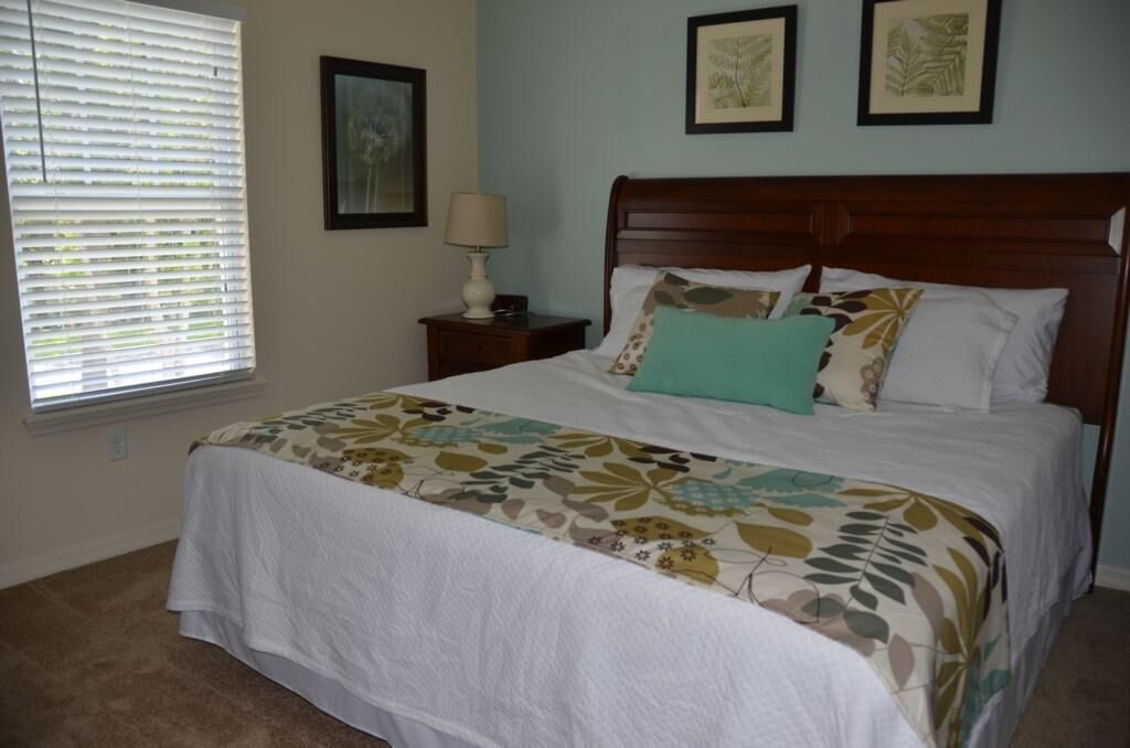 A bedroom with a large bed, a nightstand with a lamp, and two framed pictures on the wall.