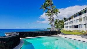 Una piscina con vistas al océano, palmeras y un edificio con balcones.