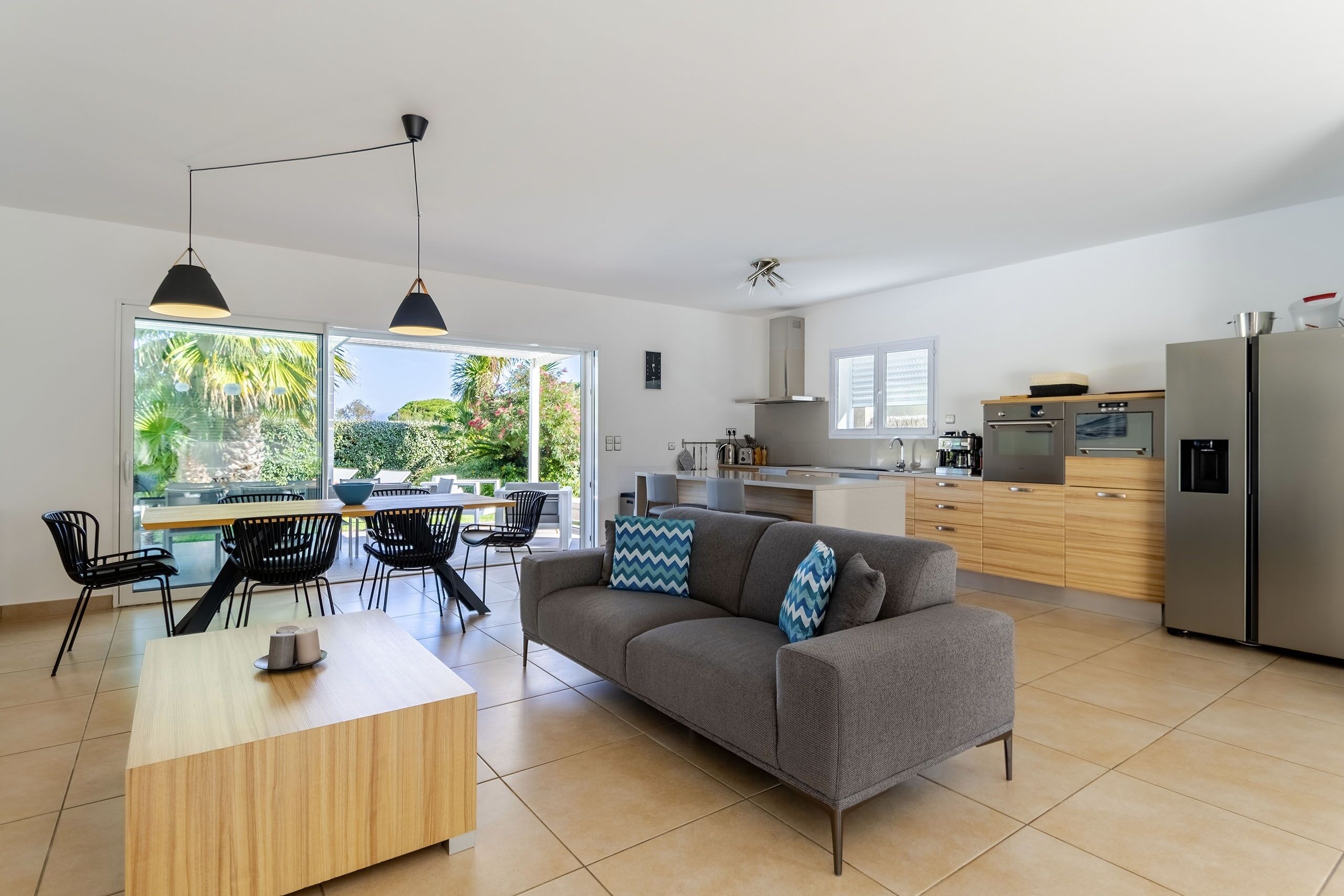 A modern kitchen with a grey sofa, wooden dining table, and black chairs.
