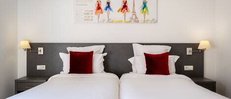 A double bed with white linens and red pillows, a grey headboard, and two bedside tables with lamps.