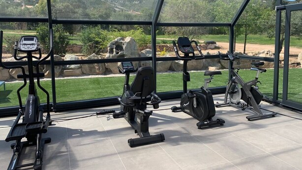 A gym with various exercise equipment, including treadmills and stationary bikes, with a view of mountains and greenery through large windows. - Exclusive Four-Bedroom Villa featuring a Private Pool, Garden, Parking and Spa (CALVI)