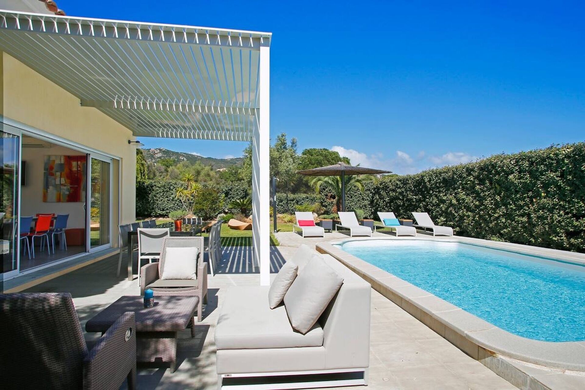 A modern outdoor pool area with lounge chairs, a covered seating area, and a view of the surrounding landscape.