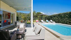 Area piscina moderna all'aperto con lettini, una zona relax coperta e vista sul paesaggio circostante.