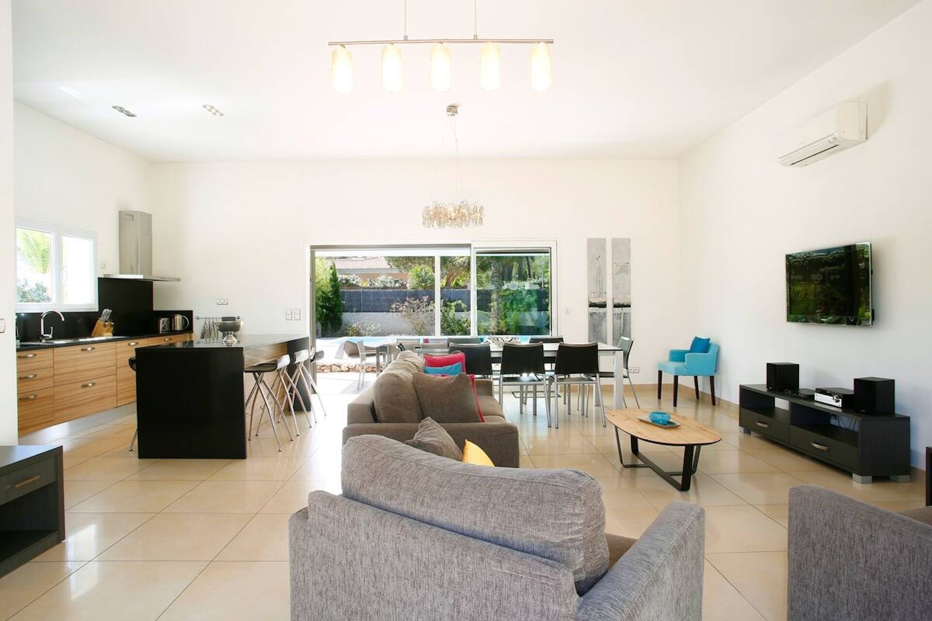 A modern living room with a sofa, coffee table, and TV. There is a kitchen area with a sink and cabinets.