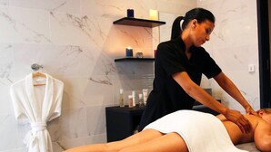 A massage therapy room with a marble-tiled wall, a towel-wrapped client, and a shelf with candles and toiletries. - Exclusive Four-Bedroom Villa featuring a Private Pool, Garden, Parking and Spa (CALVI)