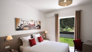 A hotel room with a large bed, a painting on the wall, a desk with a lamp, and a view of a garden through the window. - Exclusive Four-Bedroom Villa featuring a Private Pool, Garden, Parking and Spa (CALVI)