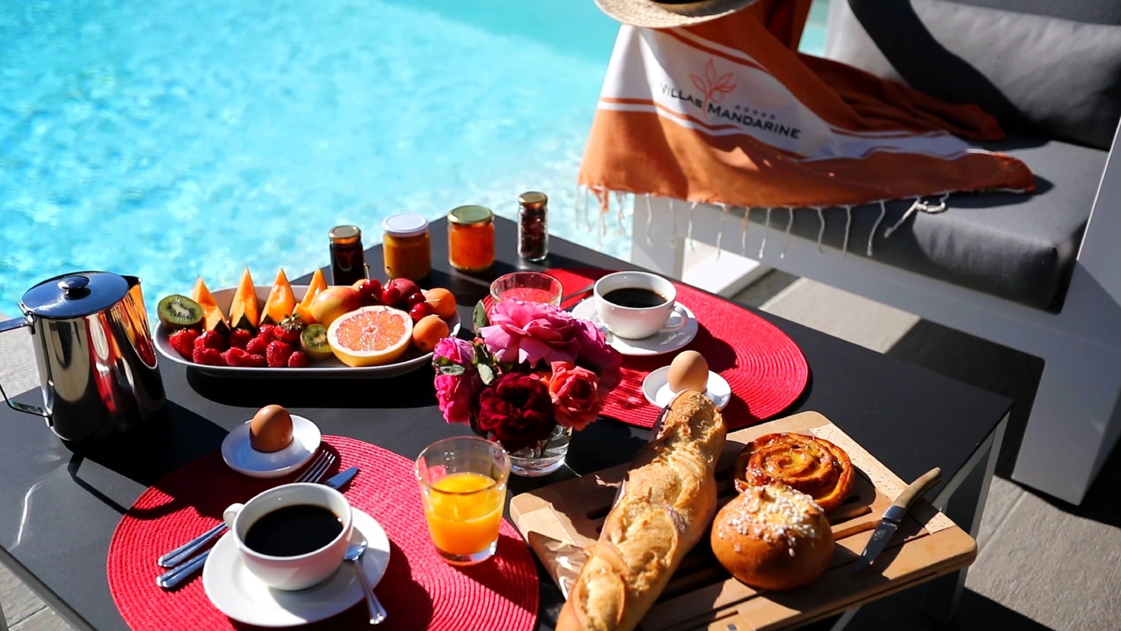 Un plateau de petit-déjeuner avec des fruits, des viennoiseries et des boissons, servi au bord de la piscine.