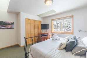 Un dormitorio con cama, almohadas, televisor, armario y un cuadro.