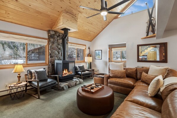 A cozy living room with a stone fireplace, leather furniture, and large windows.