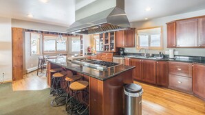 Uma cozinha moderna com armários de madeira, uma ilha central com bancos, eletrodomésticos de aço inoxidável e um exaustor grande.