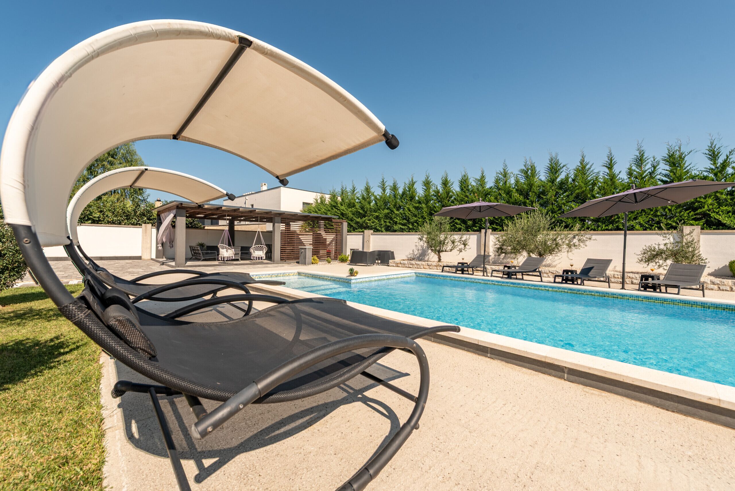 A swimming pool with lounge chairs and umbrellas, surrounded by a landscaped garden and a building with outdoor seating.