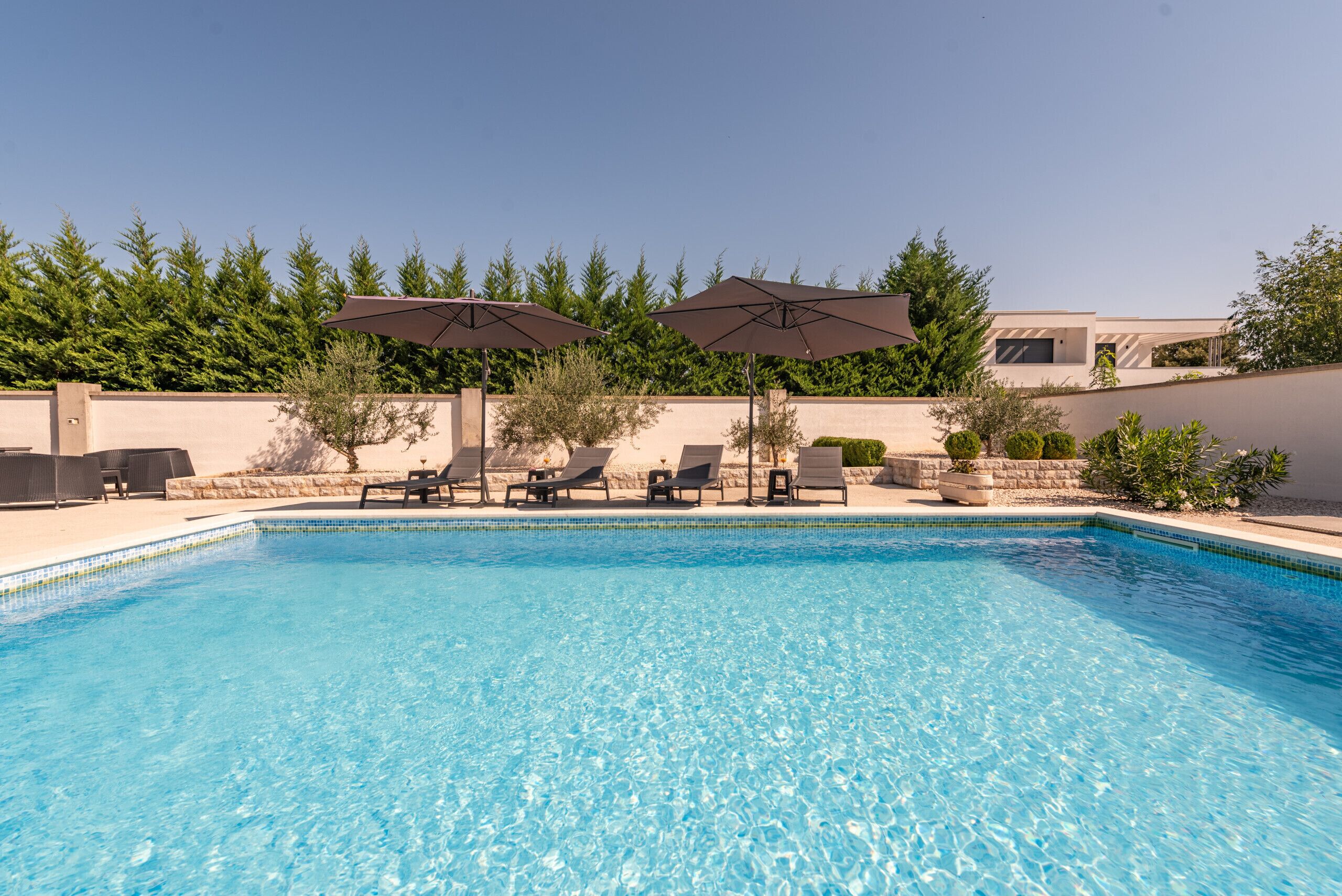 A swimming pool with lounge chairs and umbrellas, surrounded by a landscaped garden and a building in the background.