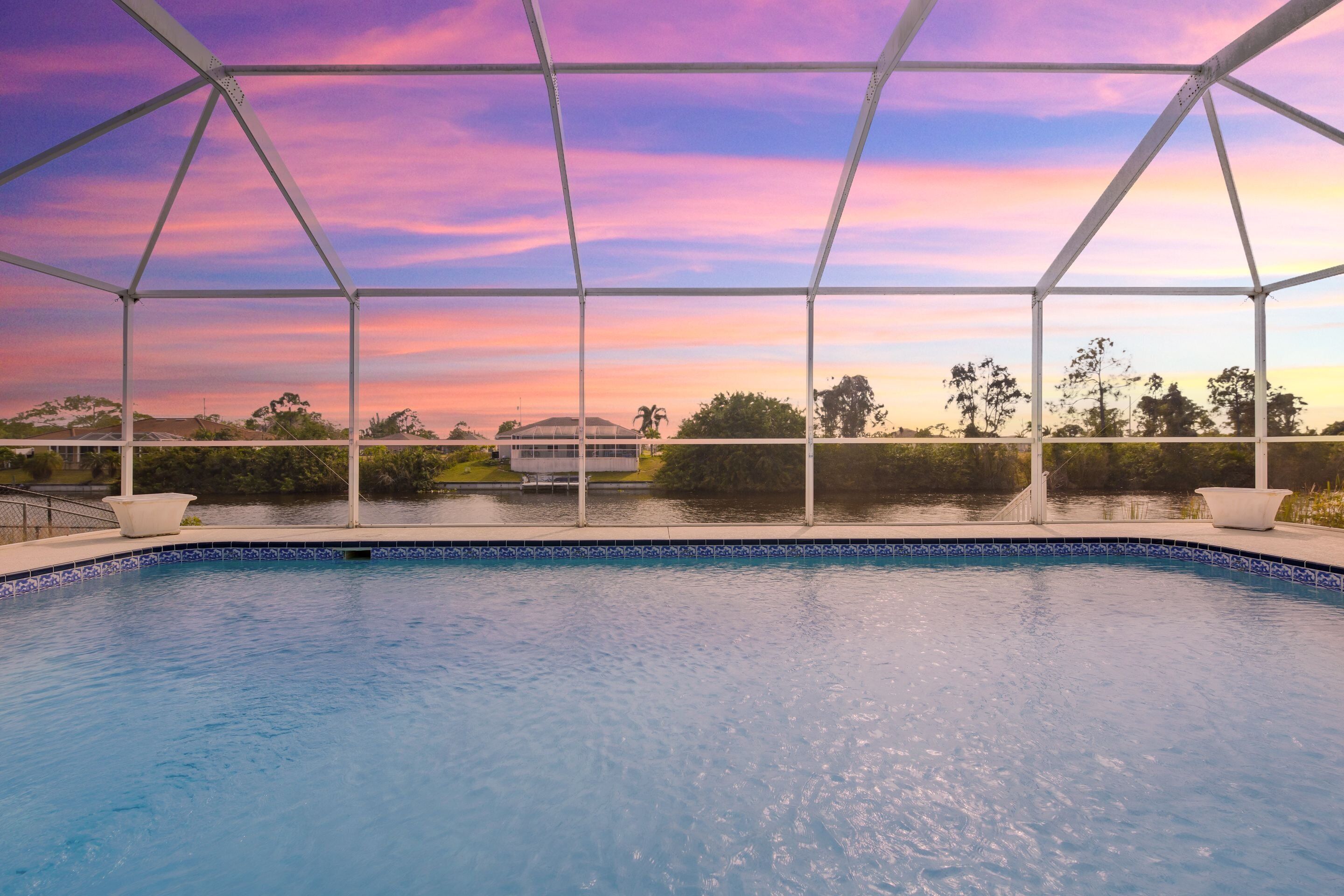 En swimmingpool med udsigt til en solnedgang over vandet, omgivet af en hvid metalstruktur.