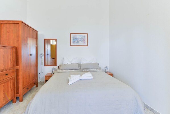 Un dormitorio con una cama, un armario de madera, una mesita de noche con una lámpara y un cuadro enmarcado en la pared.