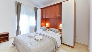A bedroom with a bed, a wooden wardrobe, two bedside lamps, and a window with curtains. - Seafront Holiday Apartment Inga Brown with sea view (Vir)