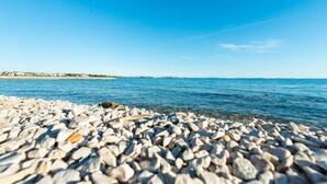 A pebble beach with a clear view of the sea and distant buildings. - Seafront Holiday Apartment Inga Brown with sea view (Vir)