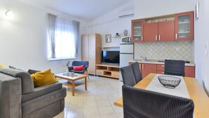 A compact living space with a sofa, a dining table with chairs, a TV, and a kitchenette with cabinets and a microwave. - Seafront Holiday Apartment Inga Brown with sea view (Vir)