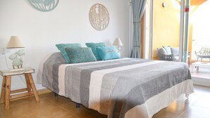 A neatly made bed with a striped bedspread and two teal pillows, a small wooden nightstand with a lamp, and a wall art piece.