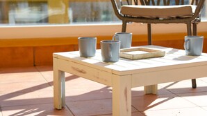 A table with four grey mugs and a tray, a wicker chair, and a window with a view of a building.