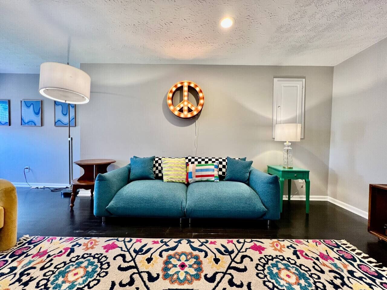 A living room with a teal sofa, patterned rug, and a peace sign light fixture.