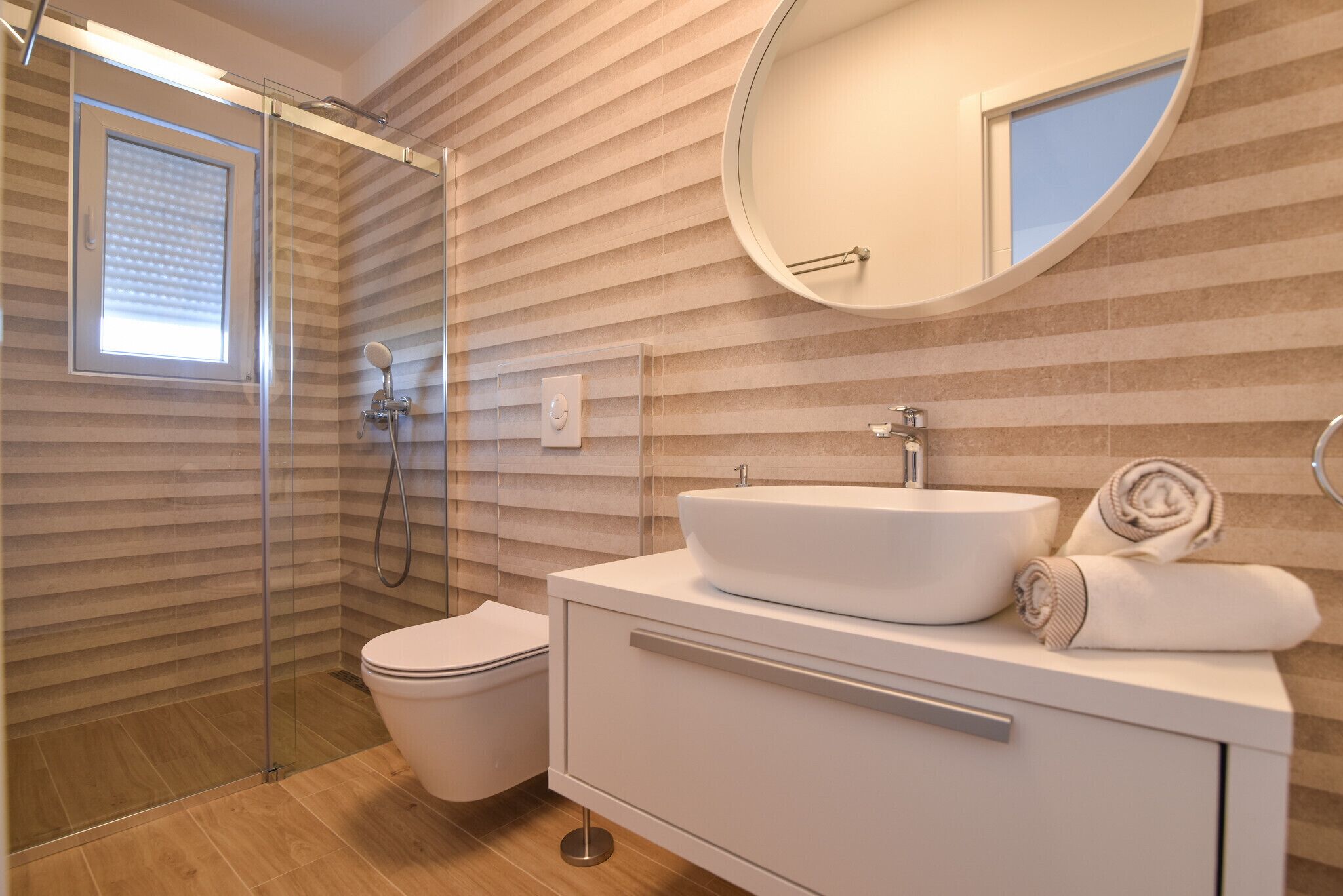 Un bagno moderno con cabina doccia in vetro, un lavandino bianco e uno specchio grande.