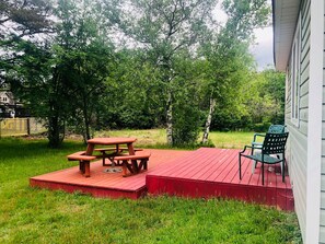 Un patio trasero con una terraza de madera roja, una mesa de picnic y una silla verde.
