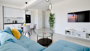 Een moderne woonkamer met een blauwe bank, een klein rond tafeltje en een aan de muur bevestigde televisie.