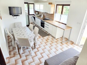 A compact kitchen with a dining area, a television mounted on the wall, and a window providing natural light.
