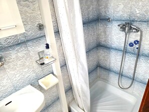 A bathroom with a shower, a sink, and a bottle of Esens body wash on a shelf.