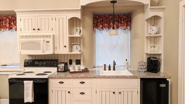 A kitchen with white cabinetry, a microwave, a stove, a refrigerator, a sink, and a coffee maker.