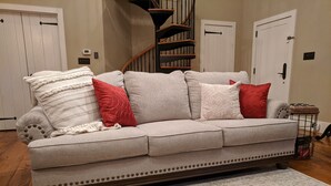A beige sectional sofa with red and white pillows, a patterned rug, and a staircase in the background.