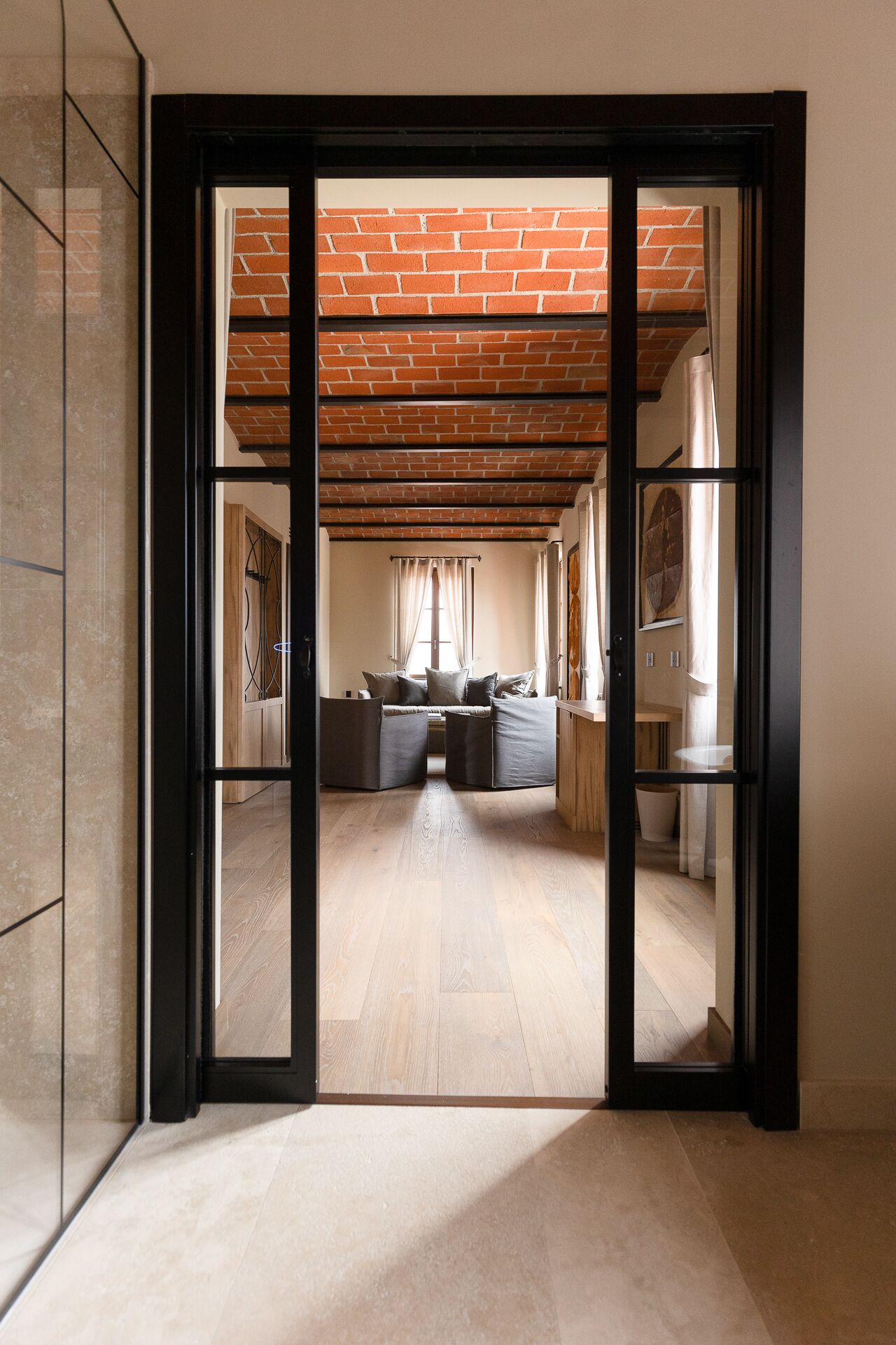 A spacious room with a brick ceiling, a wooden floor, and a seating area with a sofa and cushions.