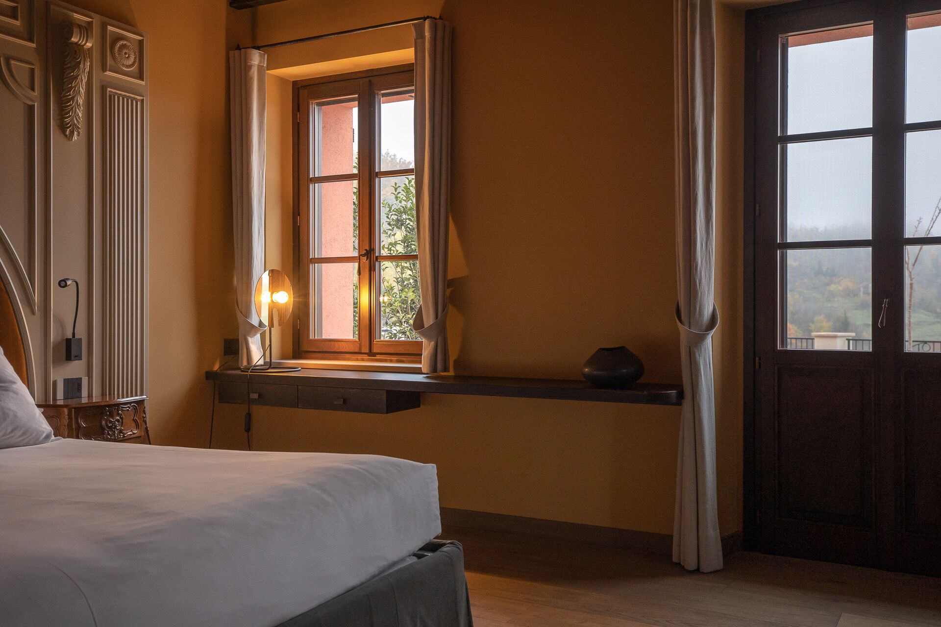 Una camera da letto con un letto, un comodino con una lampada, una finestra con tende e una porta.