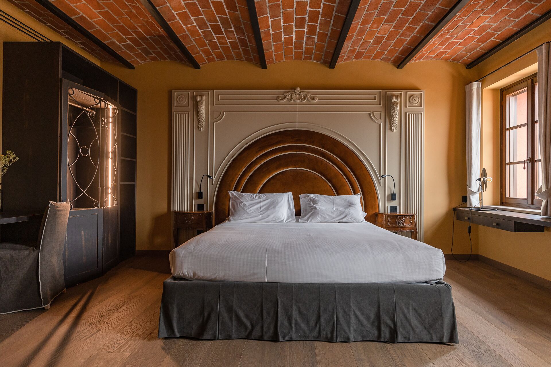 Un dormitorio con una cama grande, cabecera de madera, ventana con cortinas y techo de ladrillo.